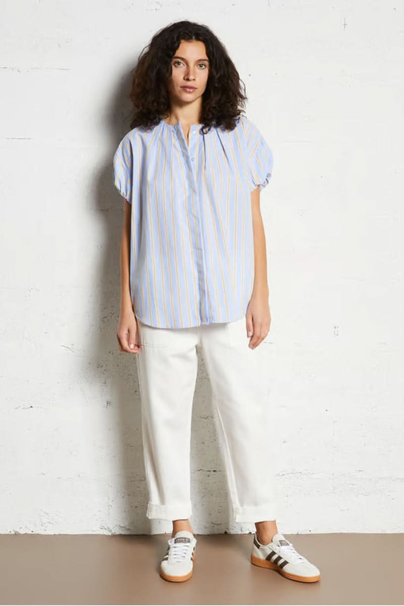 Blouse oversize à rayures bleues et jaunes, manches courtes, encolure en V, portée par une femme, style décontracté et élégant.