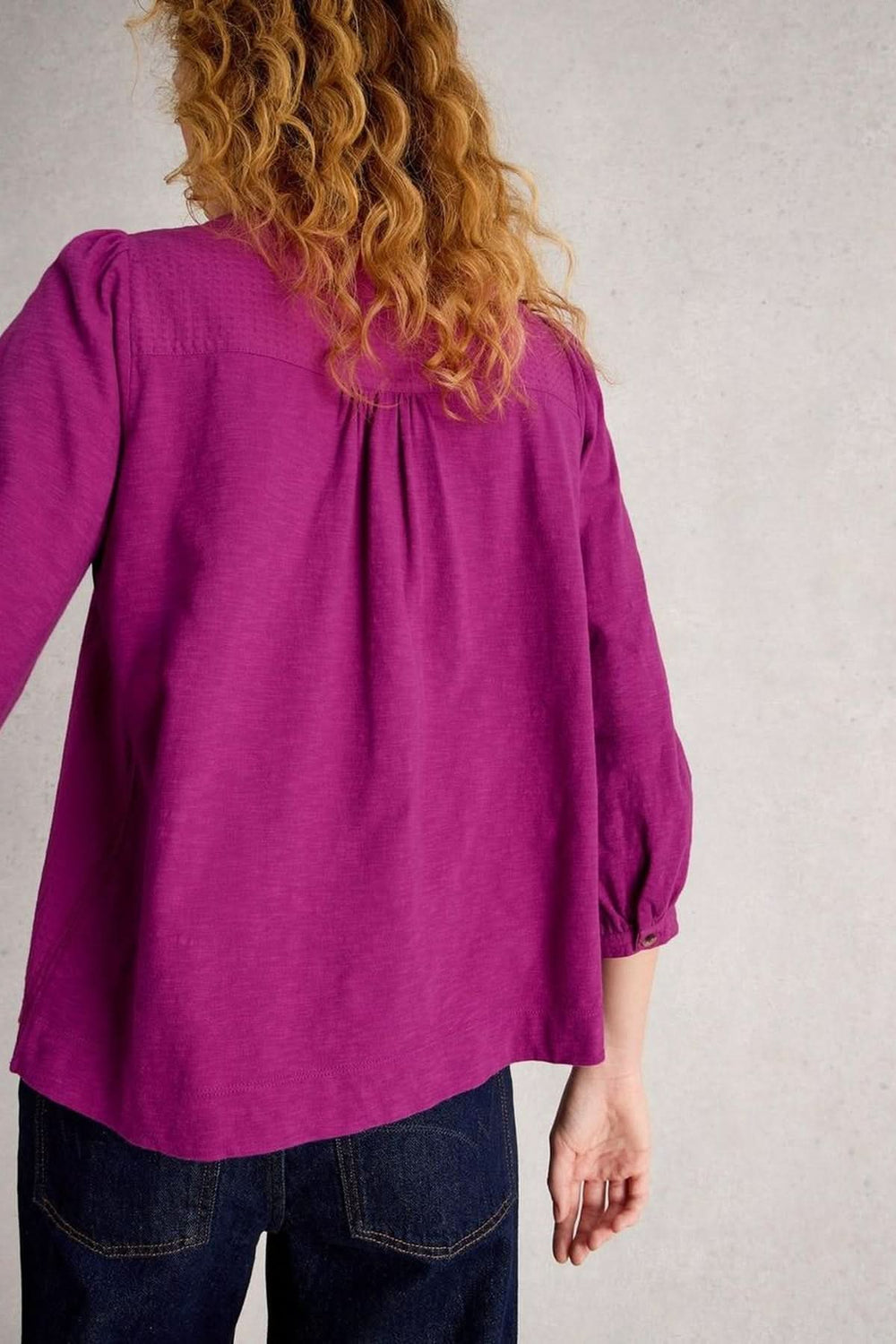 Femme portant une blouse plumetis à plastron froncé violette avec texture légère, assortie à un jean, vue de dos.