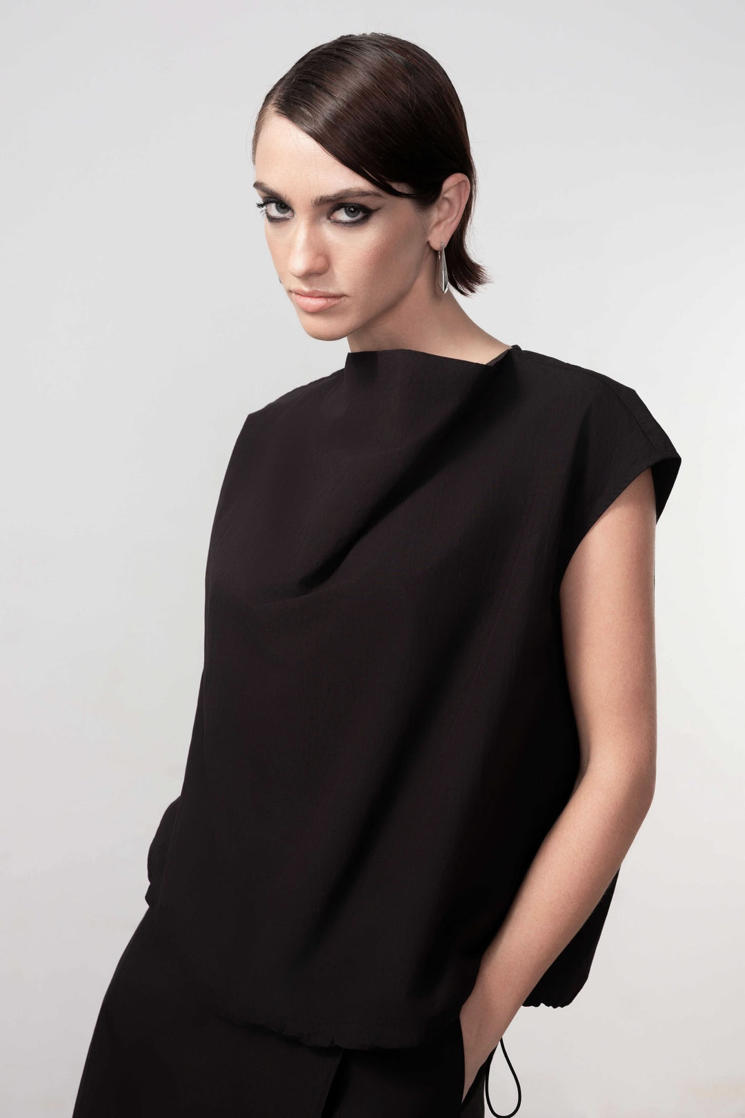 Blouse sans manches avec design épuré et drapé subtil, coupe droite fluide pour une élégance moderne, modèle féminin en noir.