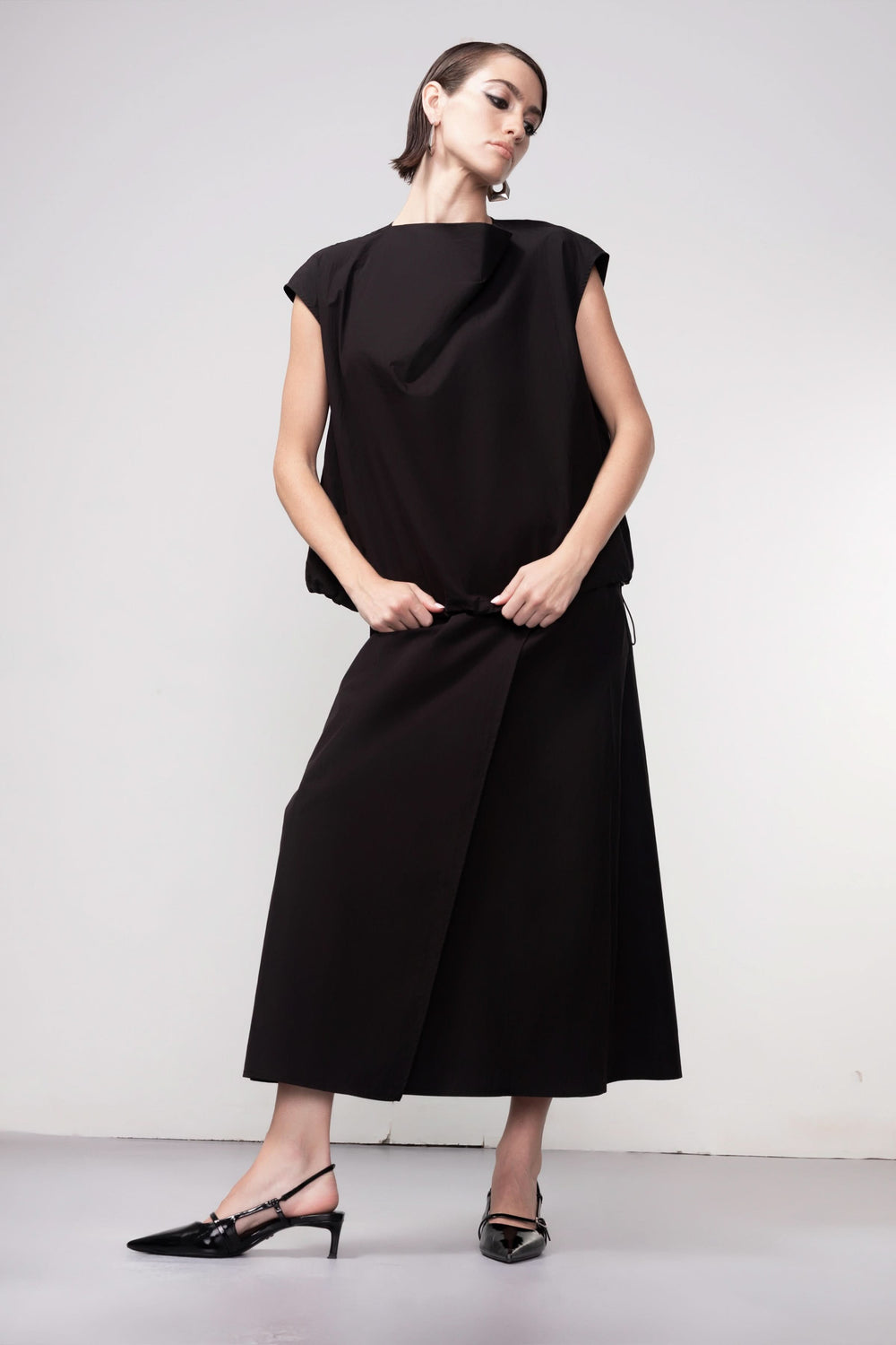 Femme portant une blouse sans manches avec design épuré et coupe fluide, illustrant élégance et modernité.