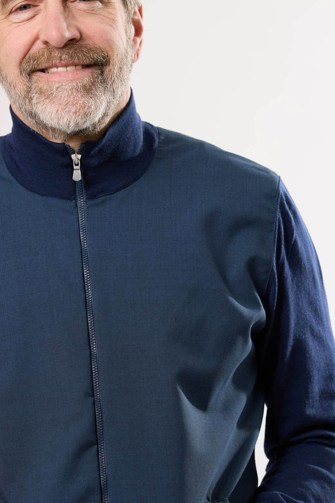 Homme souriant portant un blouson sportif bleu avec col montant et fermeture éclair.