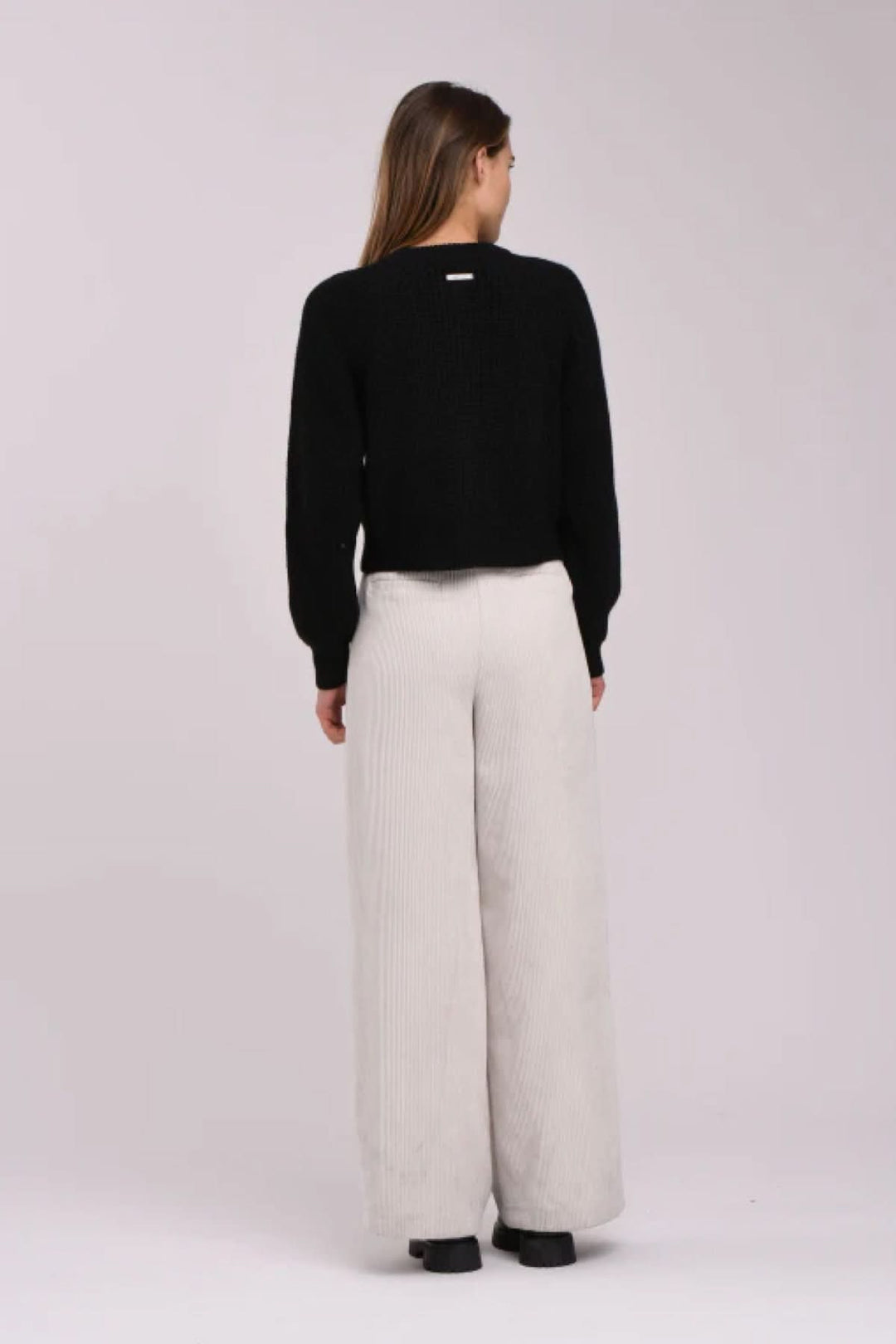 Femme de dos portant un cardigan noir élégant et un pantalon large en beige, montrant une tenue chic et confortable.