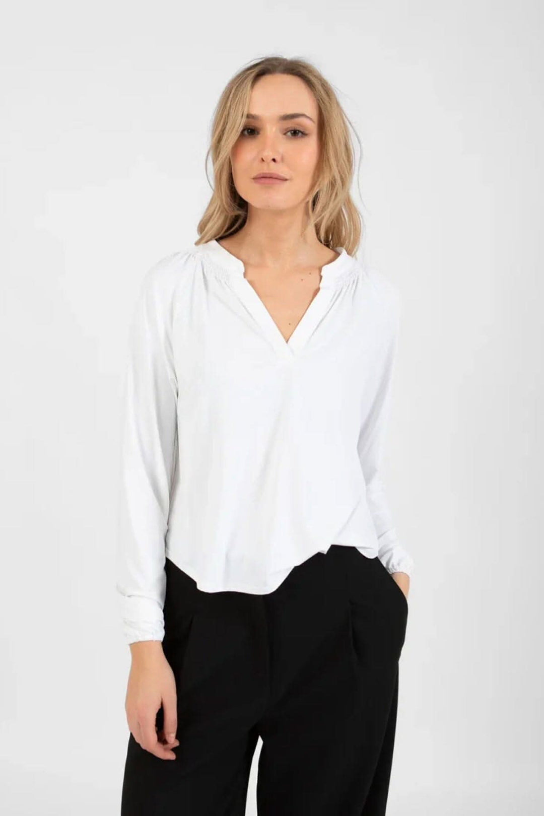 Chandail ample blanc avec détails smockés, col V, porté par un mannequin en pantalon noir.