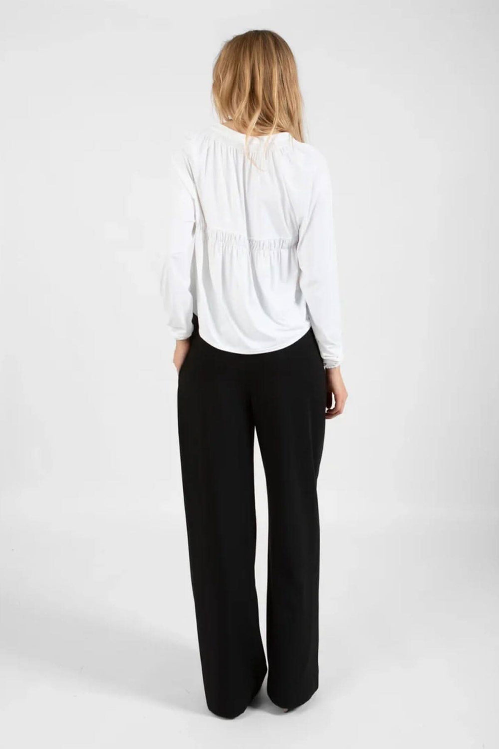 Chandail ample blanc avec détail smocké au dos porté avec un pantalon noir, vue de dos.