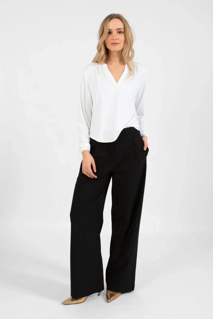 Chandail ample blanc avec détails smockés au dos, porté avec un pantalon noir, look élégant.