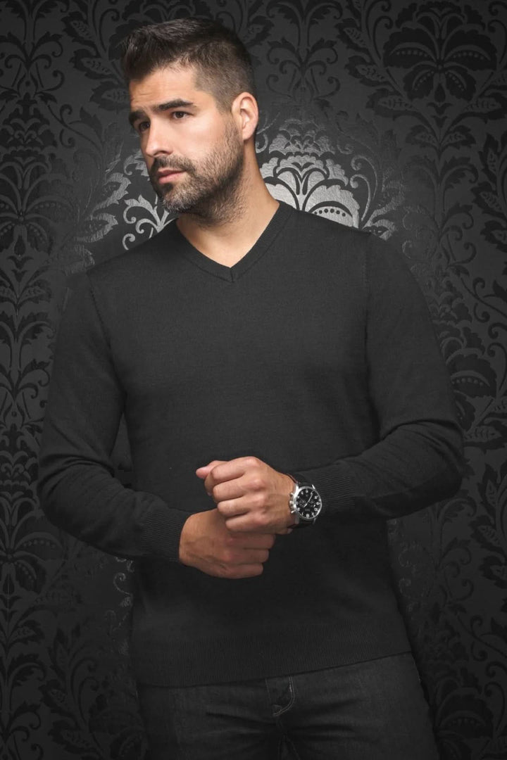 Homme portant un chandail en laine SAXONY noir avec un col en V, contre un fond décoratif.