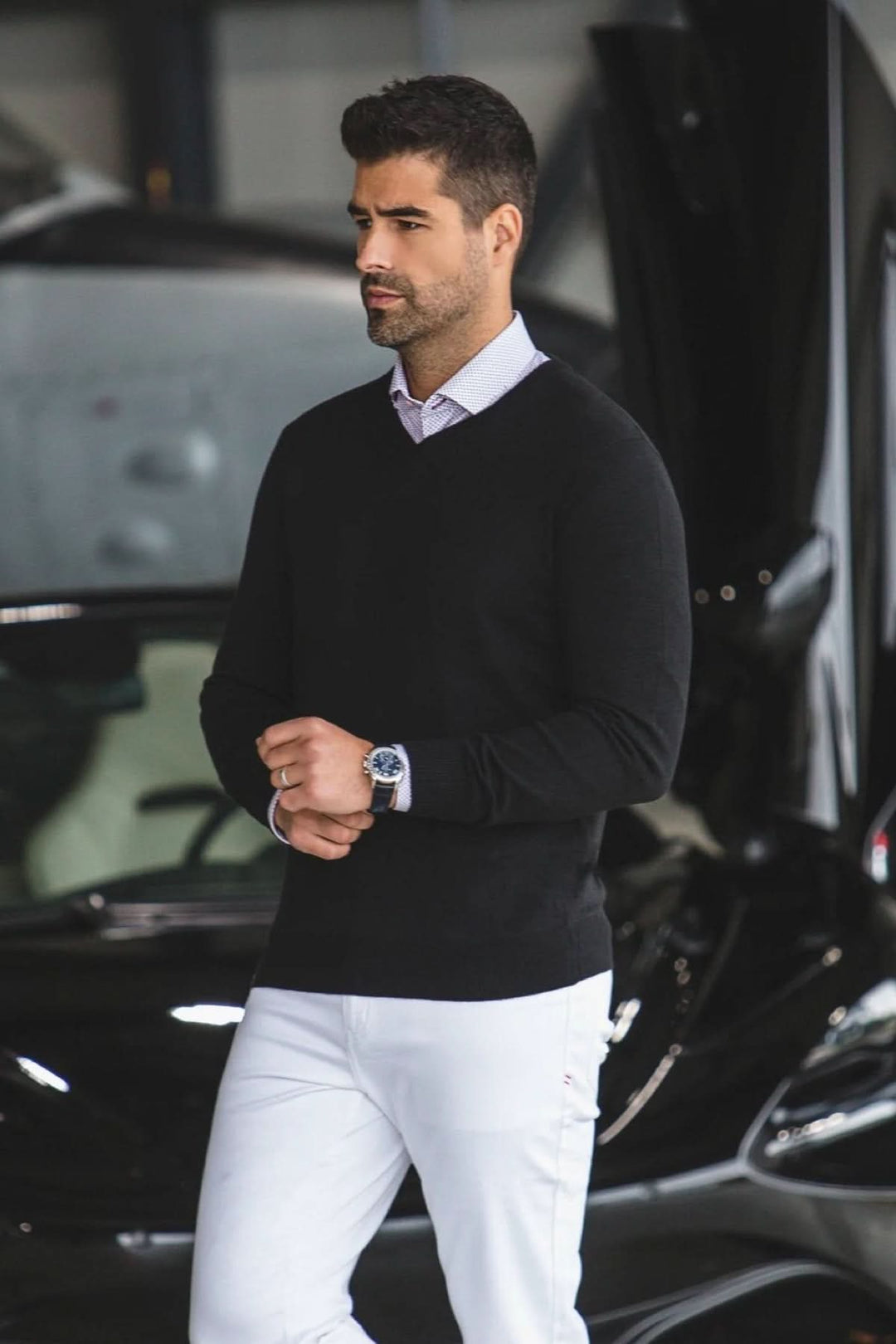 Homme portant un chandail en laine SAXONY noir, élégant et moderne, devant une voiture de luxe.