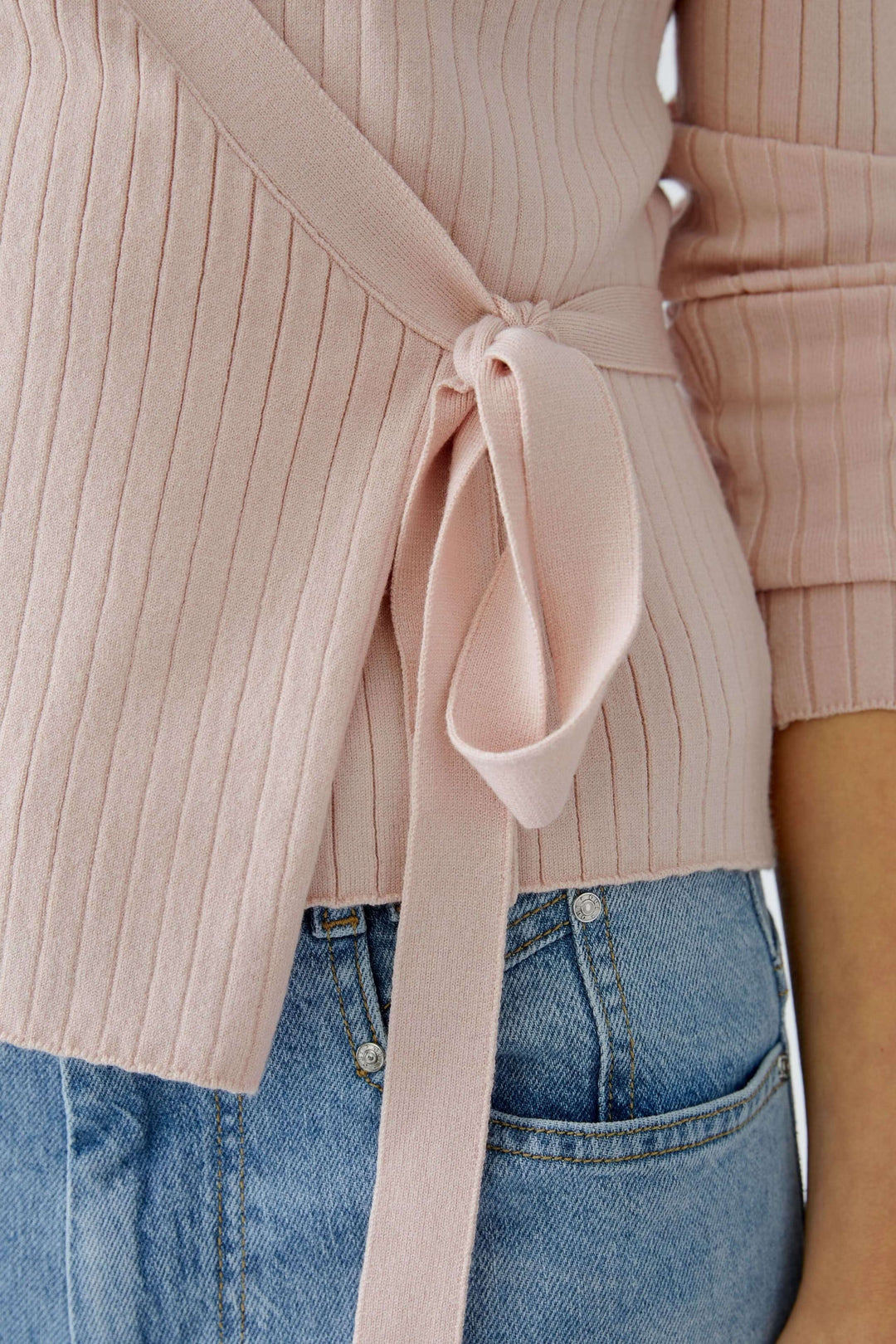 Cache-cœur en maille rose avec lien noué sur le côté, mettant en valeur une silhouette féminine et raffinée.
