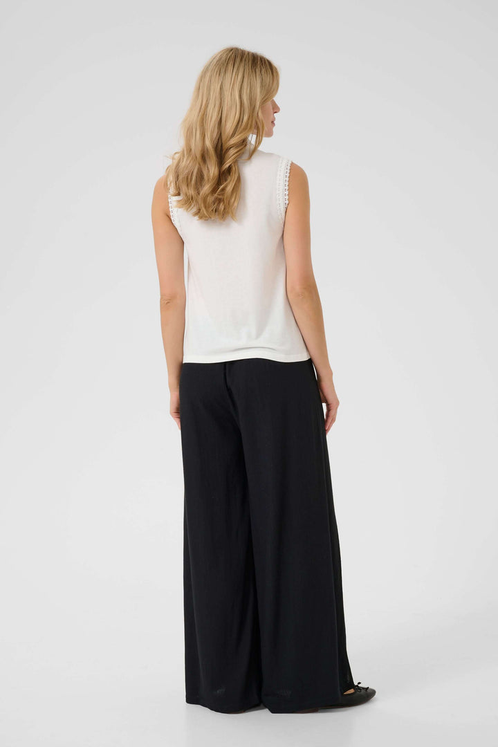 Femme portant une camisole sans manches blanche avec un pantalon noir fluide, vue de dos.