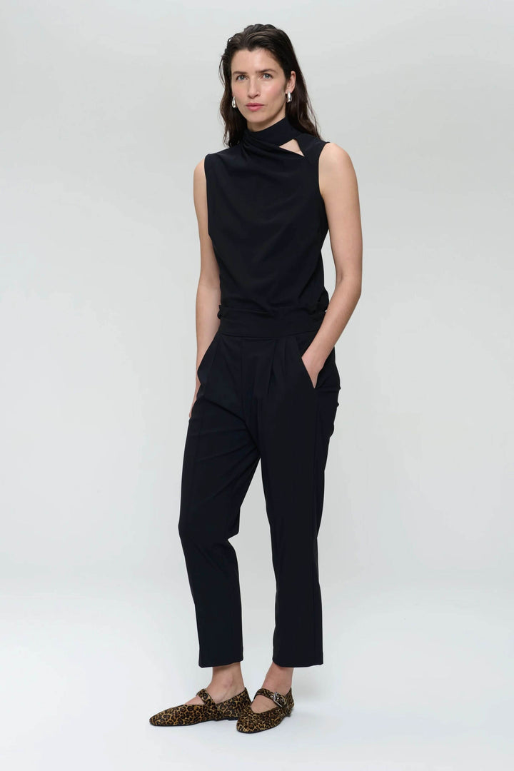 Camisole Naomi noire avec col drapé et ouverture asymétrique, portée avec un pantalon noir élégant.
