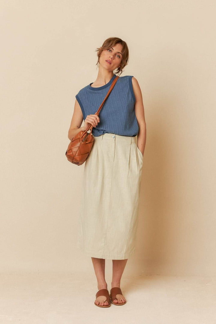 Femme en camisole ample bleue avec jupe longue beige et sac en cuir, look décontracté et élégant.