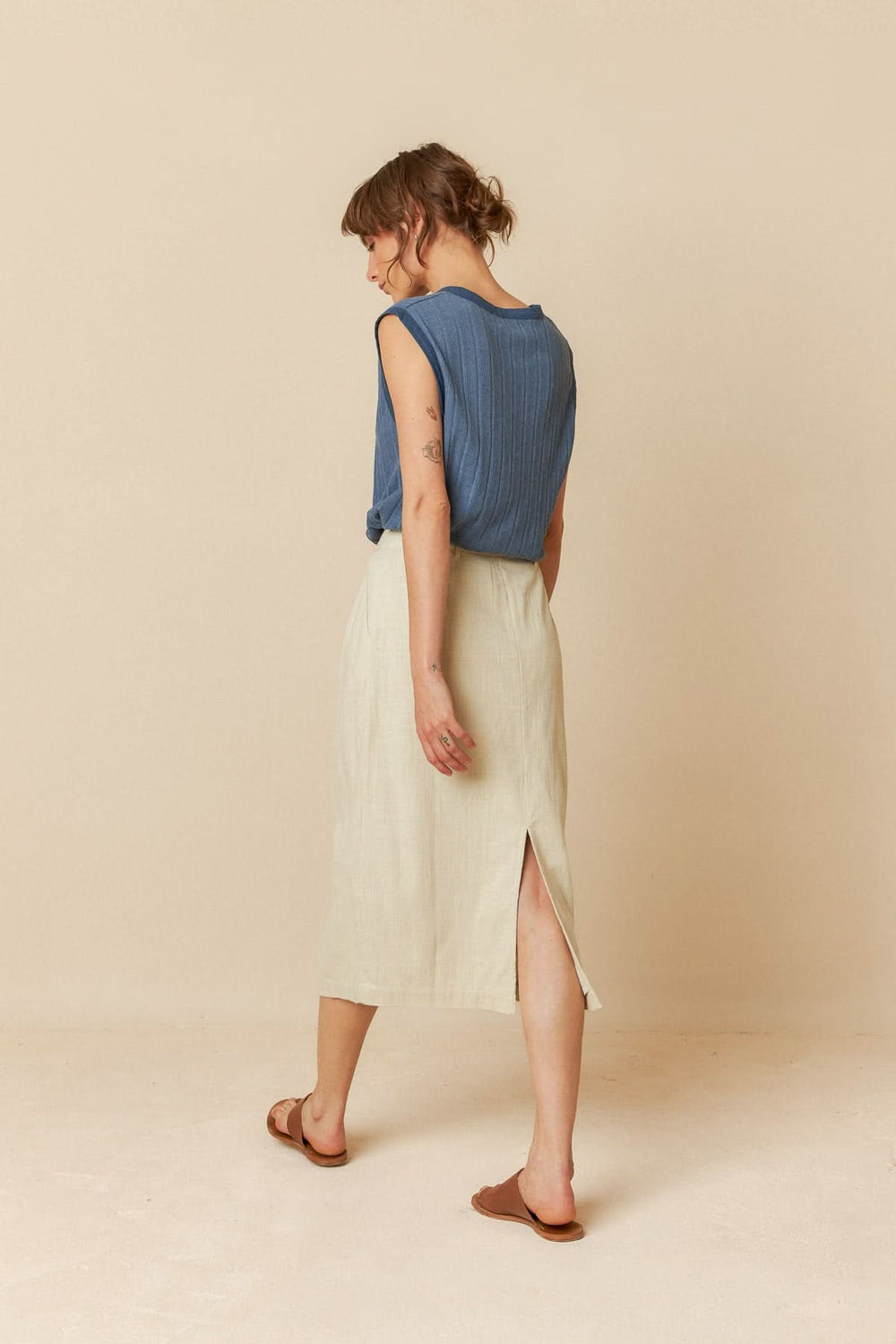 Femme de dos portant une camisole ample bleu et une jupe midi beige, parfaite pour les journées chaudes.