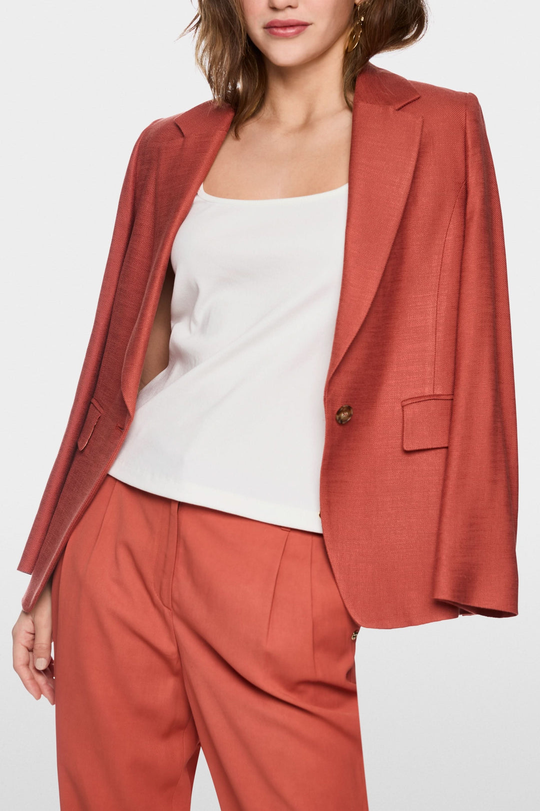 Femme portant une camisole à encolure carrée blanche sous une veste corail, ensemble élégant et moderne, style minimaliste.