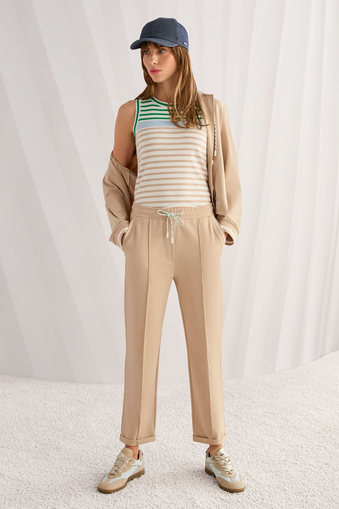 Femme portant une camisole rayé en coton avec encolure ronde contrastante, associée à un pantalon beige et une casquette bleue.
