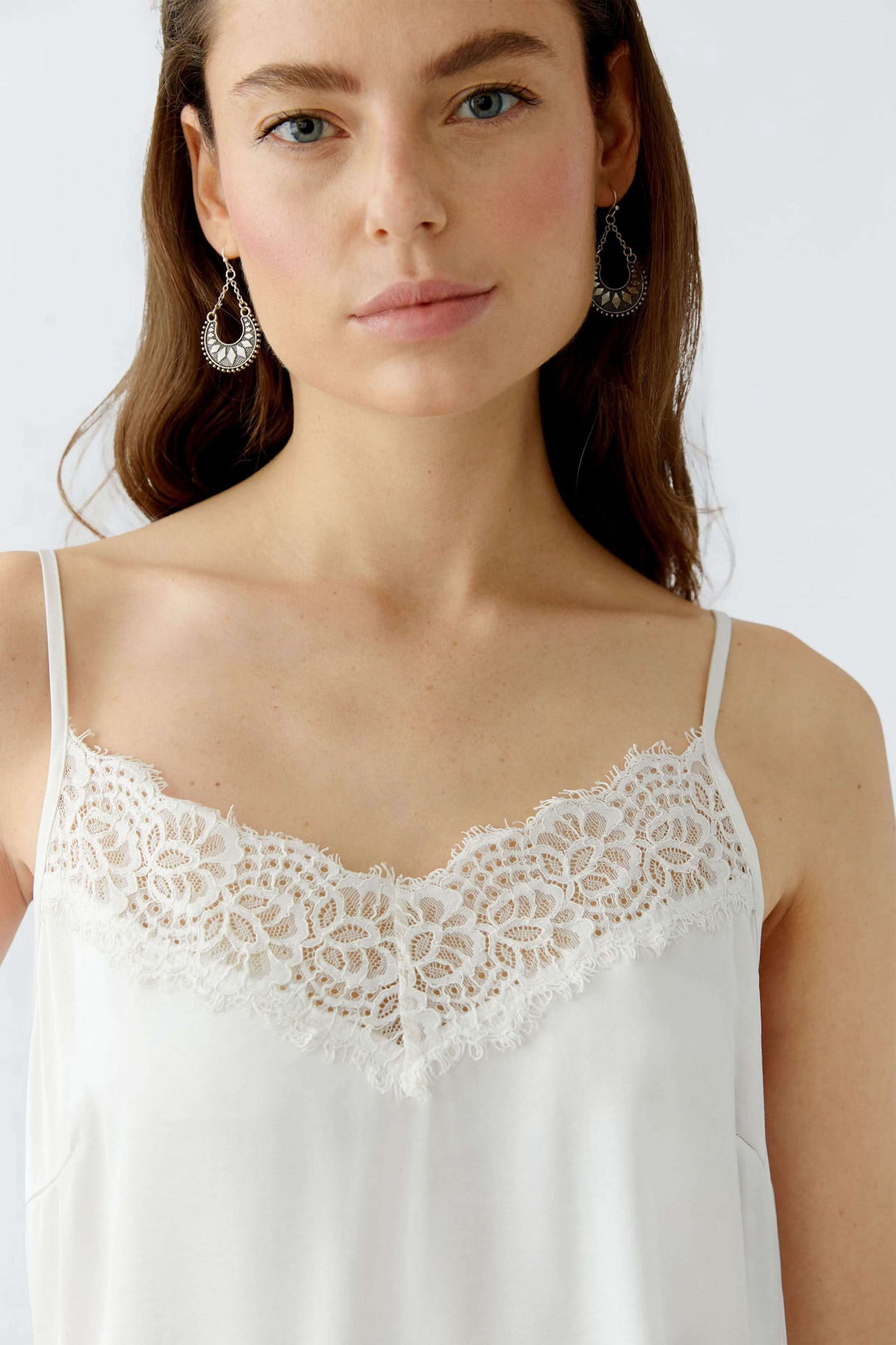 Camisole satin blanc avec dentelle délicate à l'encolure, décolleté en V et bretelles spaghetti.