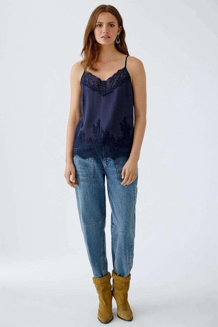 Camisole satin marine avec dentelle ornée, décolleté en V et bretelles spaghetti, portée avec un jean et des bottes.