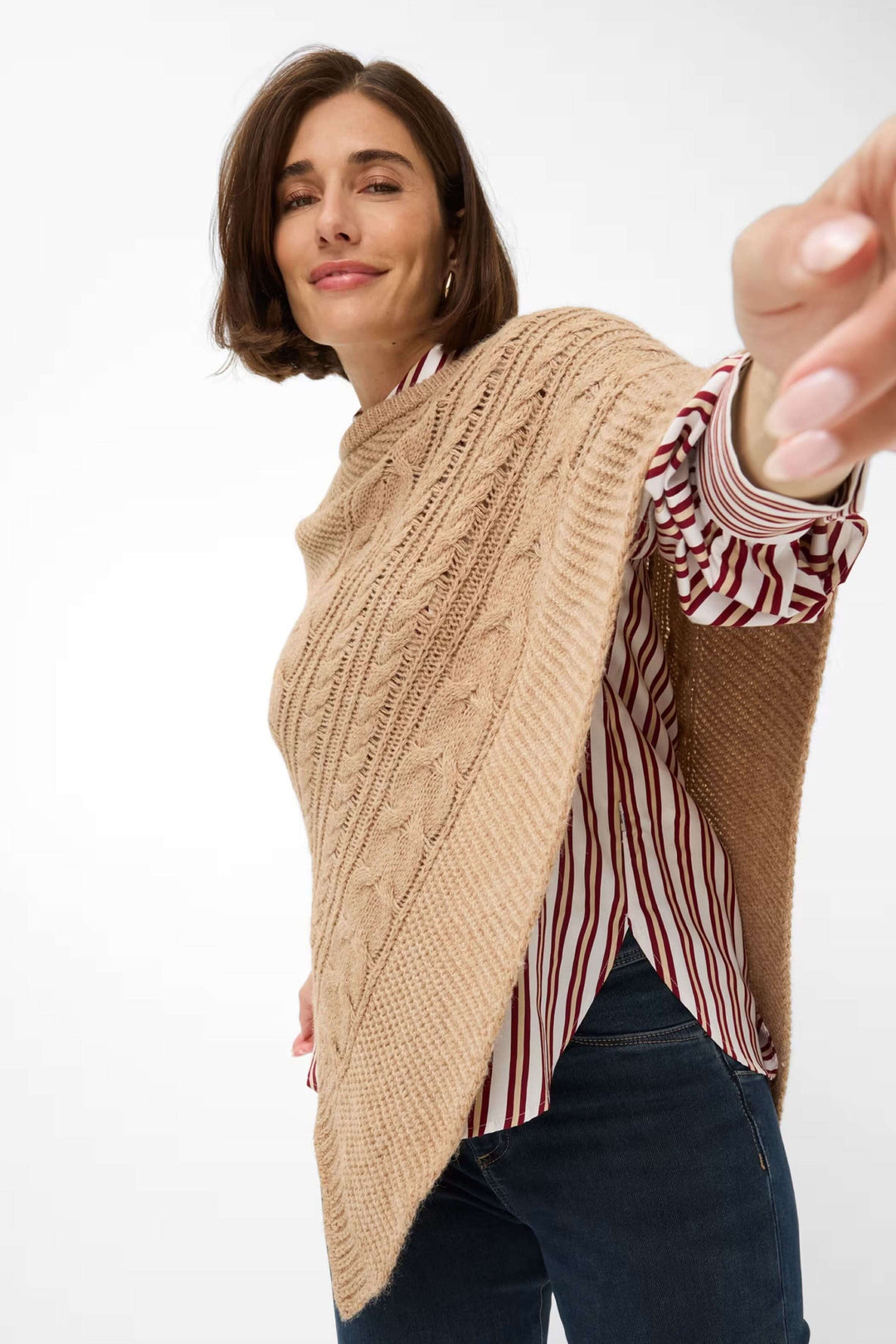 Femme portant la Cape Thea en tricot torsadé beige avec un motif texturé et une coupe asymétrique élégante.