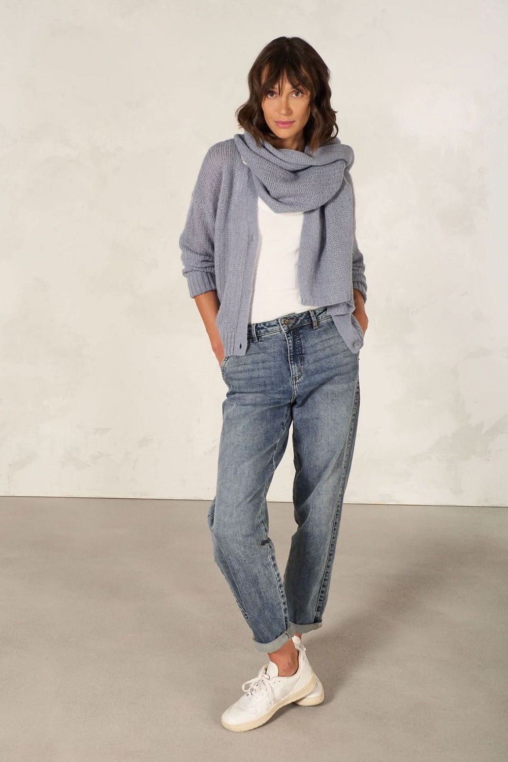 Femme portant un tricot multifonctionnel bleu comme écharpe avec un pantalon en jean décontracté.