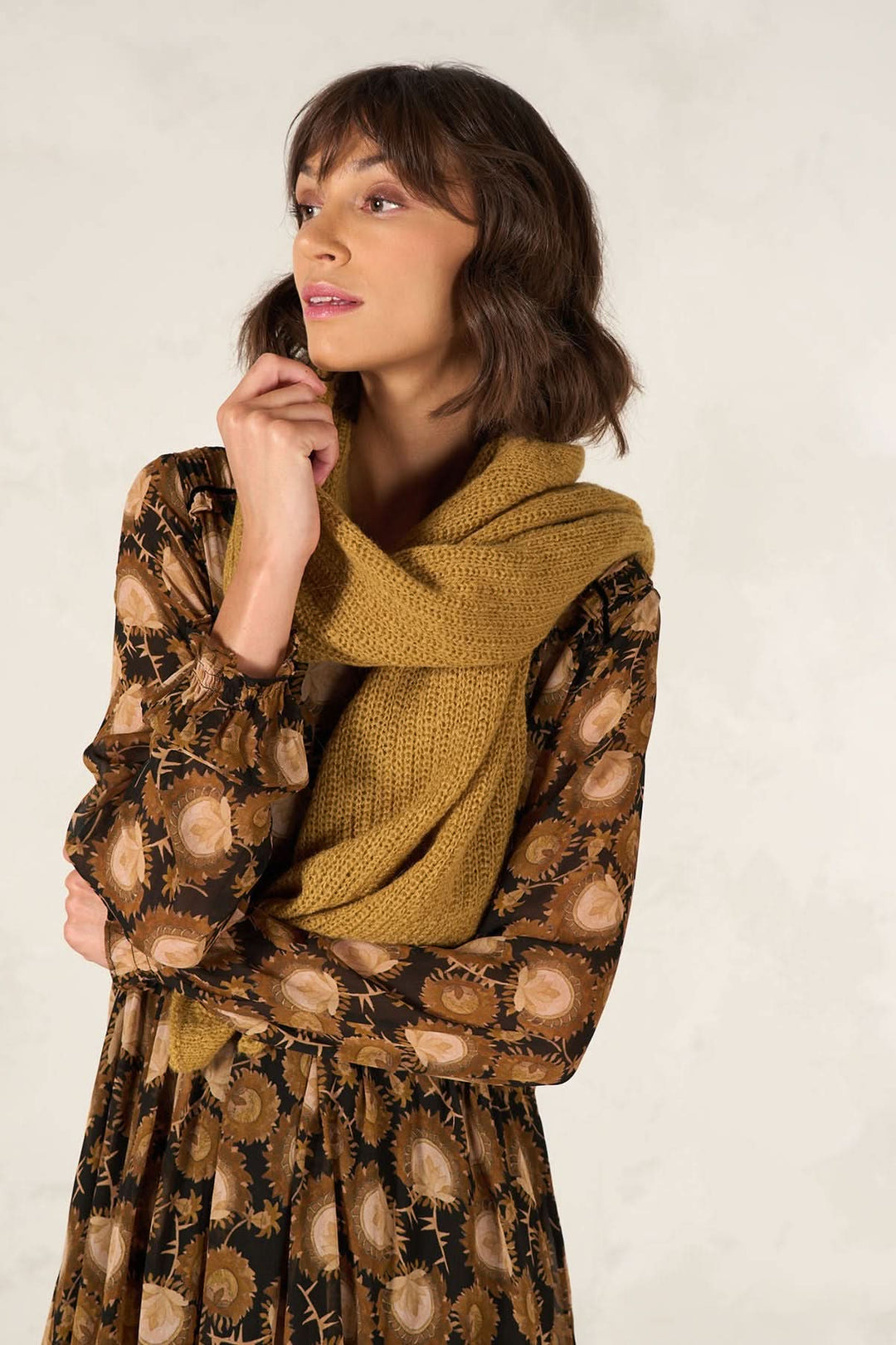 Modèle portant une cape foulard jaune en tricot, associée à une robe à motifs floraux.