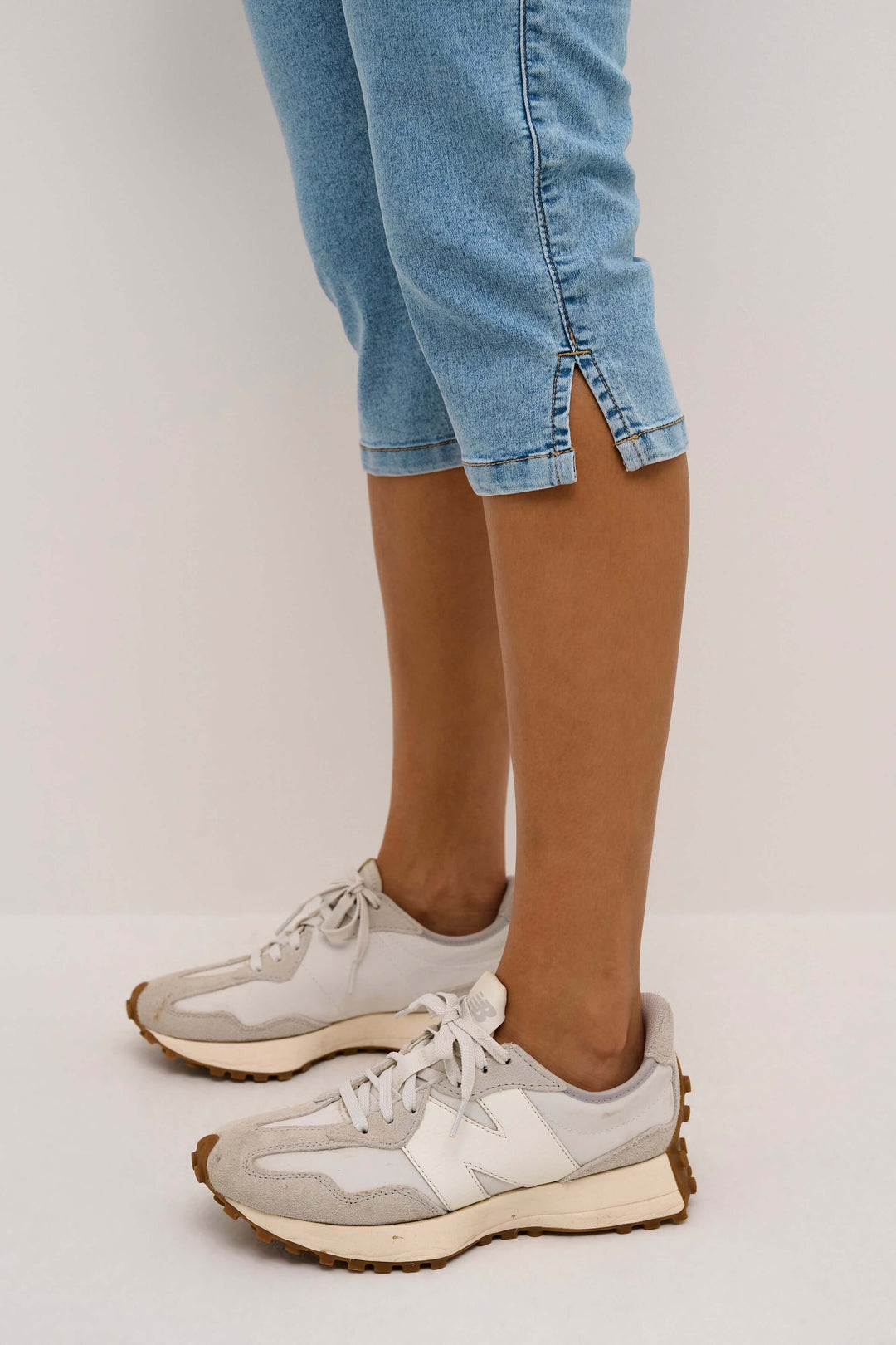 Femme portant un capri en denim extensible avec des sneakers modernes, détail de la coupe ajustée et longueur sous le genou.