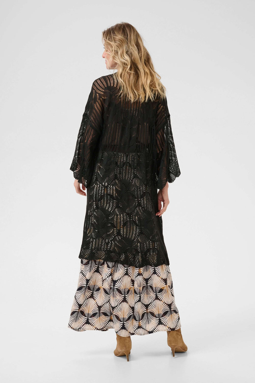 Cardigan Franca long en tricot ajouré noir, fluide, porté sur une jupe à motifs floraux.