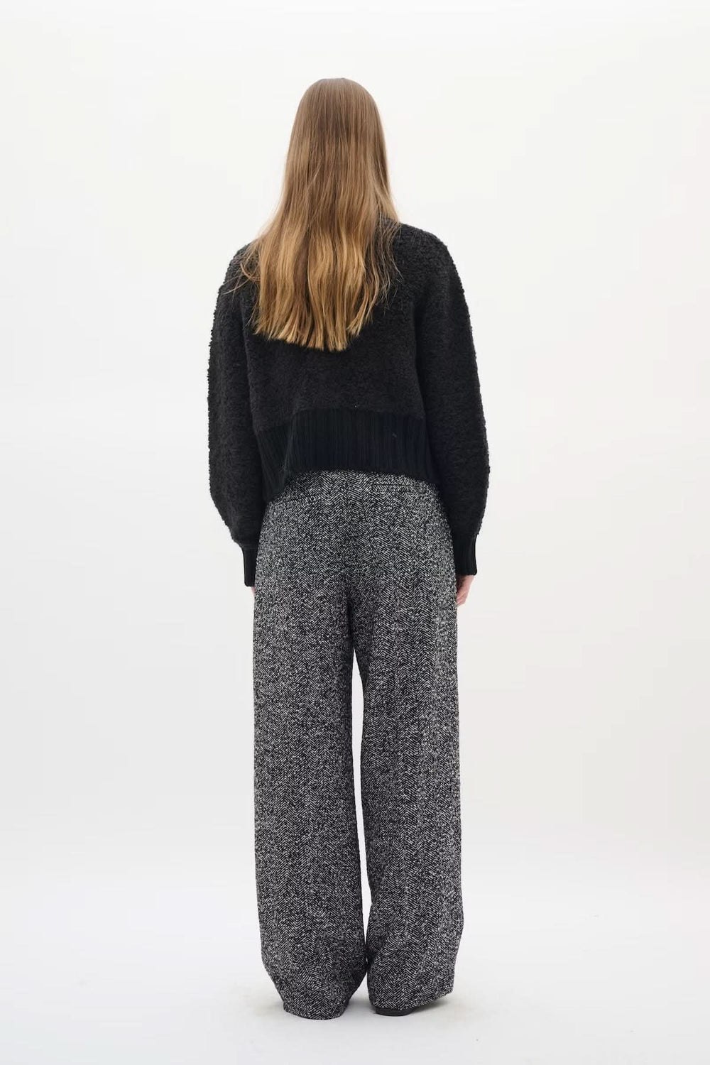 Person wearing Cardigan Guo, black textured knit with golden buttons, styled with high-waist pants for a chic silhouette from the back.