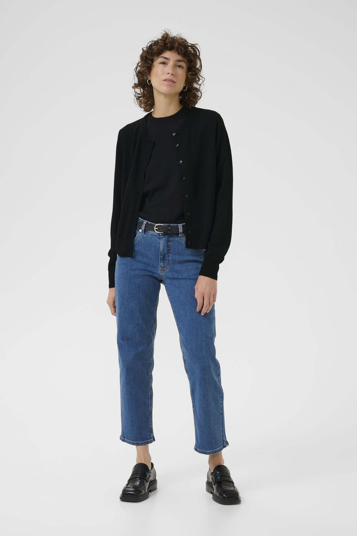 Femme portant un cardigan noir classique avec encolure ronde sur un T-shirt, associé à un jean bleu élégant.