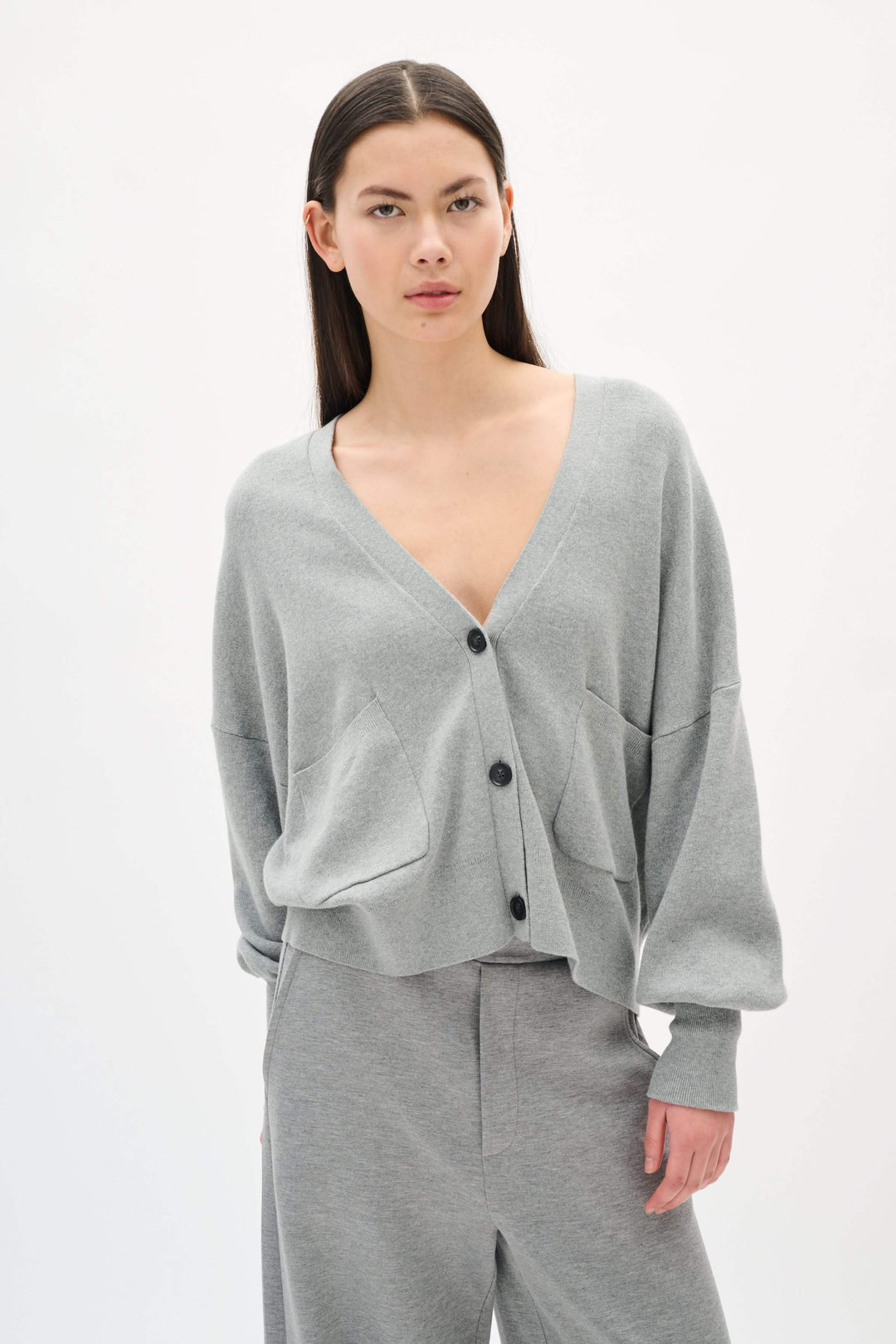 Cardigan Tenley ample en gris avec encolure en V, poche avant et boutons contrastants, porté avec pantalon gris.