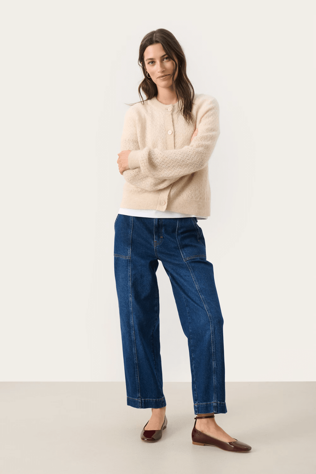 Femme portant un Cardigan Thora beige à encolure ronde avec un jean bleu pour un look décontracté chic.