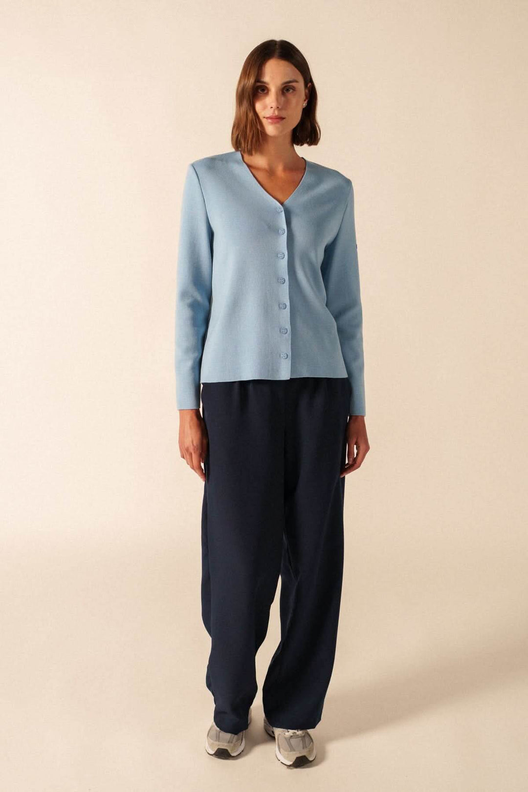 Femme portant un Cardigan de laine BREVANDS bleu avec encolure en V et boutons discrets sur un pantalon sombre en studio.