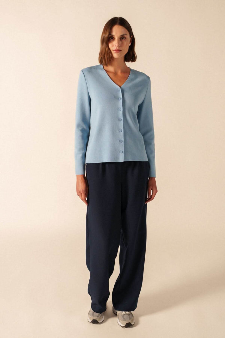 Femme portant un Cardigan de laine BREVANDS bleu avec encolure en V et boutons discrets sur un pantalon sombre en studio.