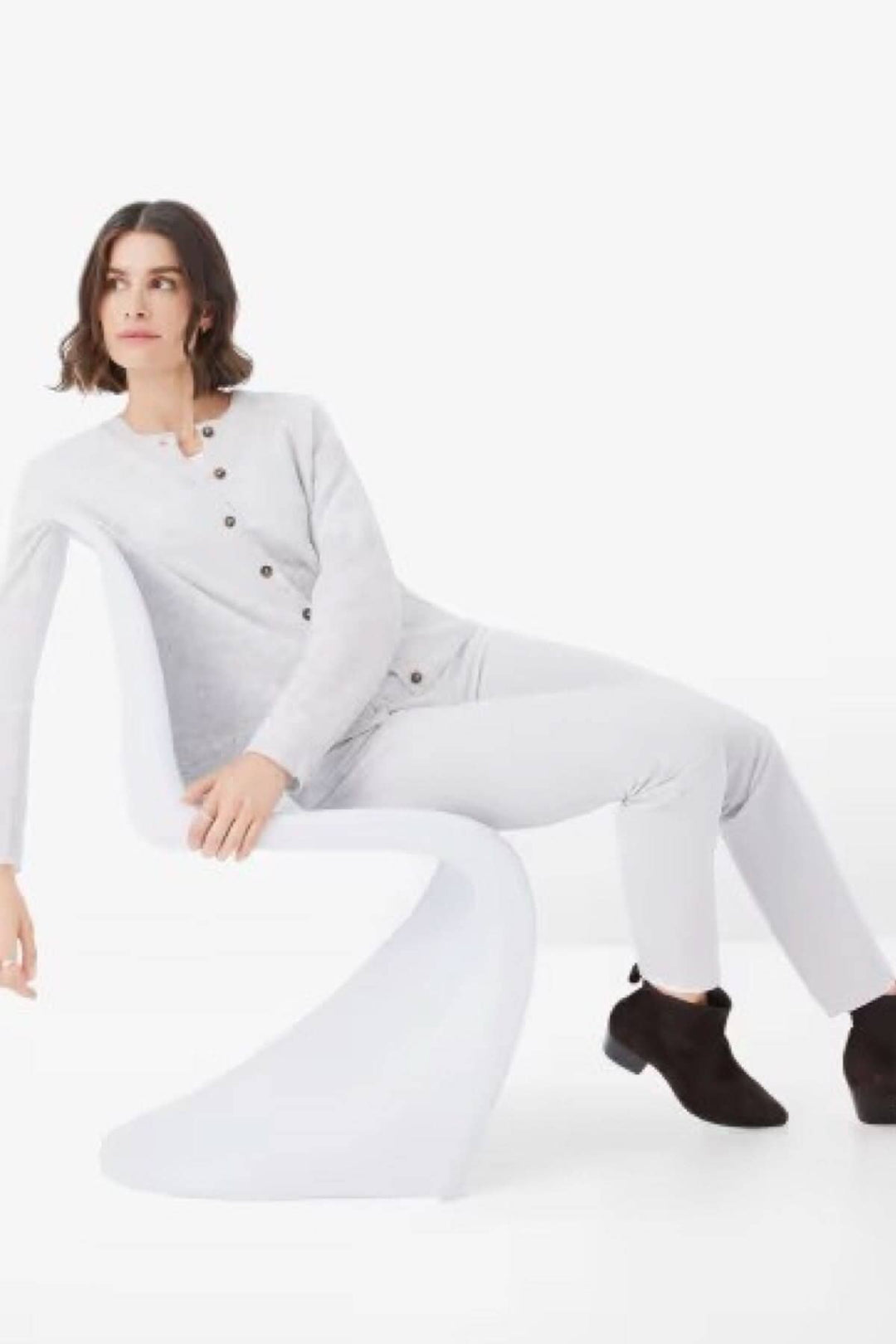 Femme en cardigan gris assise sur une chaise moderne, montrant un style décontracté et élégant.