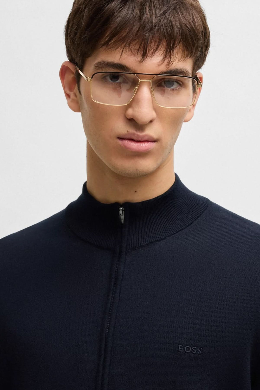 Homme portant un cardigan en maille noir avec logo BOSS brodé, col montant et lunettes élégantes.