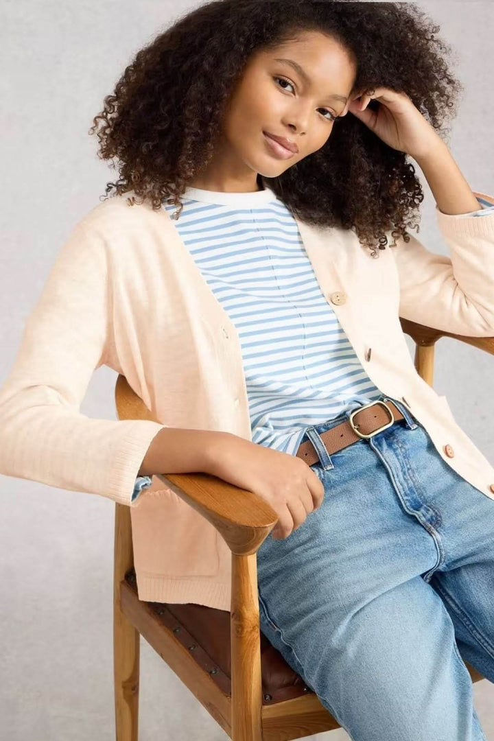 Femme portant le Cardigan en mélange de lin Nova avec jean et t-shirt à rayures, assise sur une chaise en bois, look décontracté.