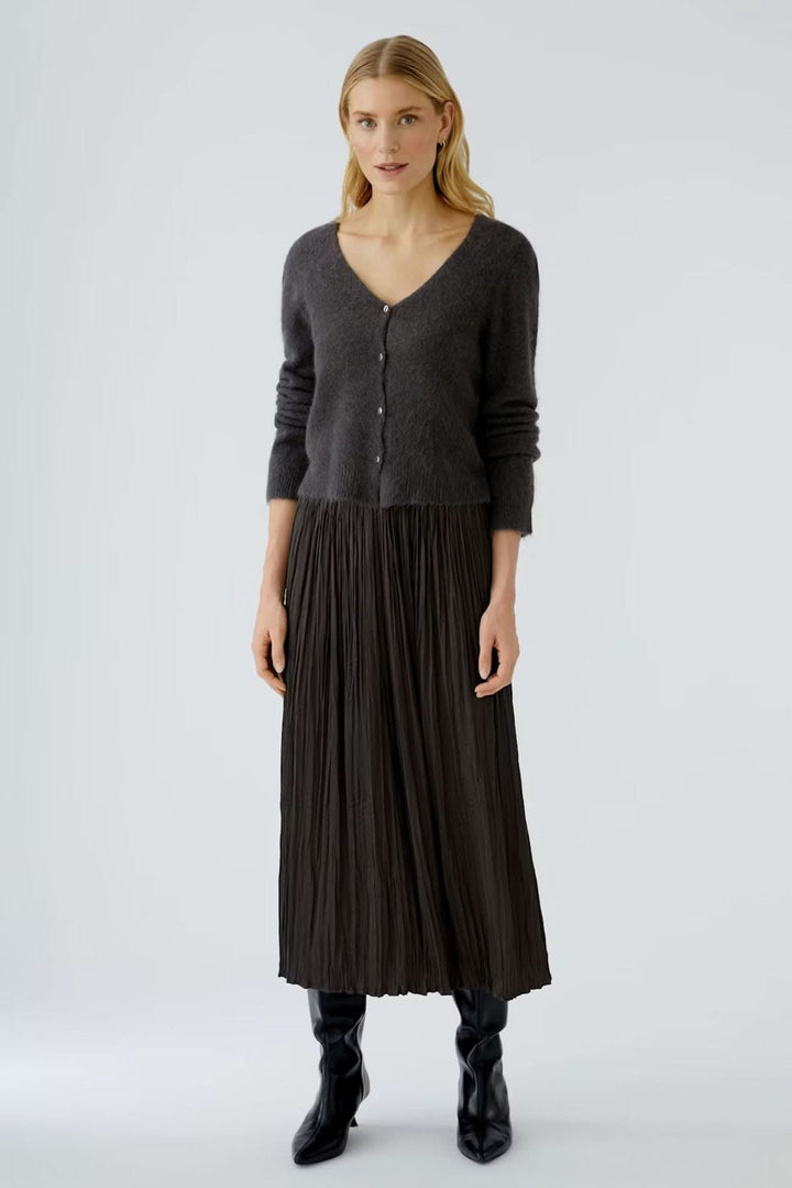 Femme portant un cardigan à encolure en V en maille duveteuse avec boutons contrastés, associé à une jupe plissée et des bottes noires.