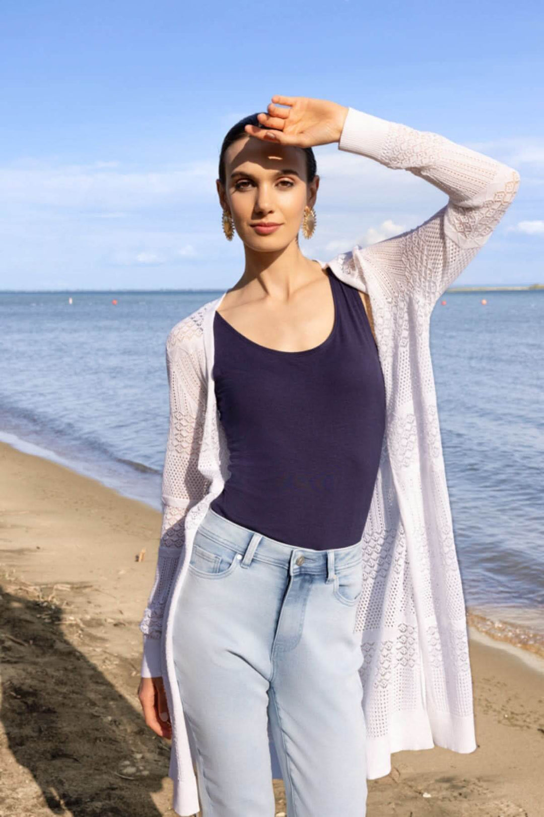 Modèle portant un cardigan long en maille ajourée sur une plage, tenue casual chic.