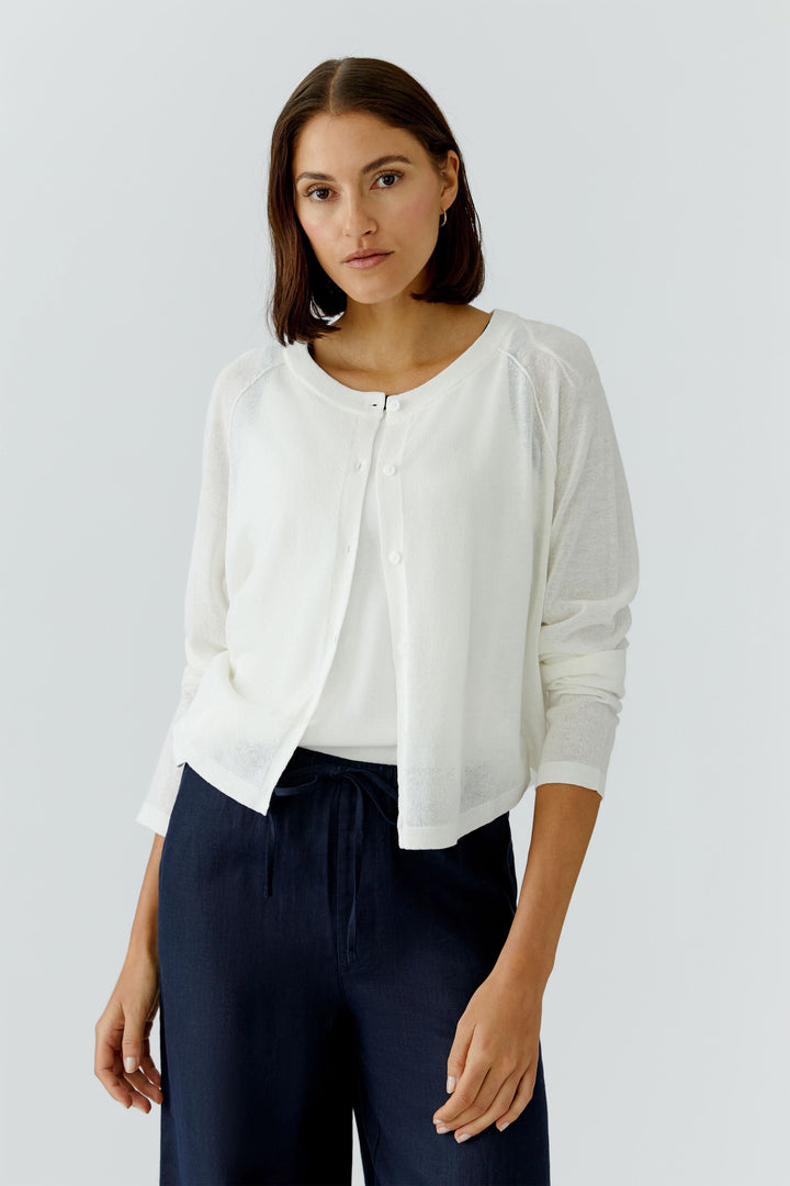 Femme portant un cardigan texturé boutonné blanc à encolure arrondie, parfait pour un style élégant et féminin.