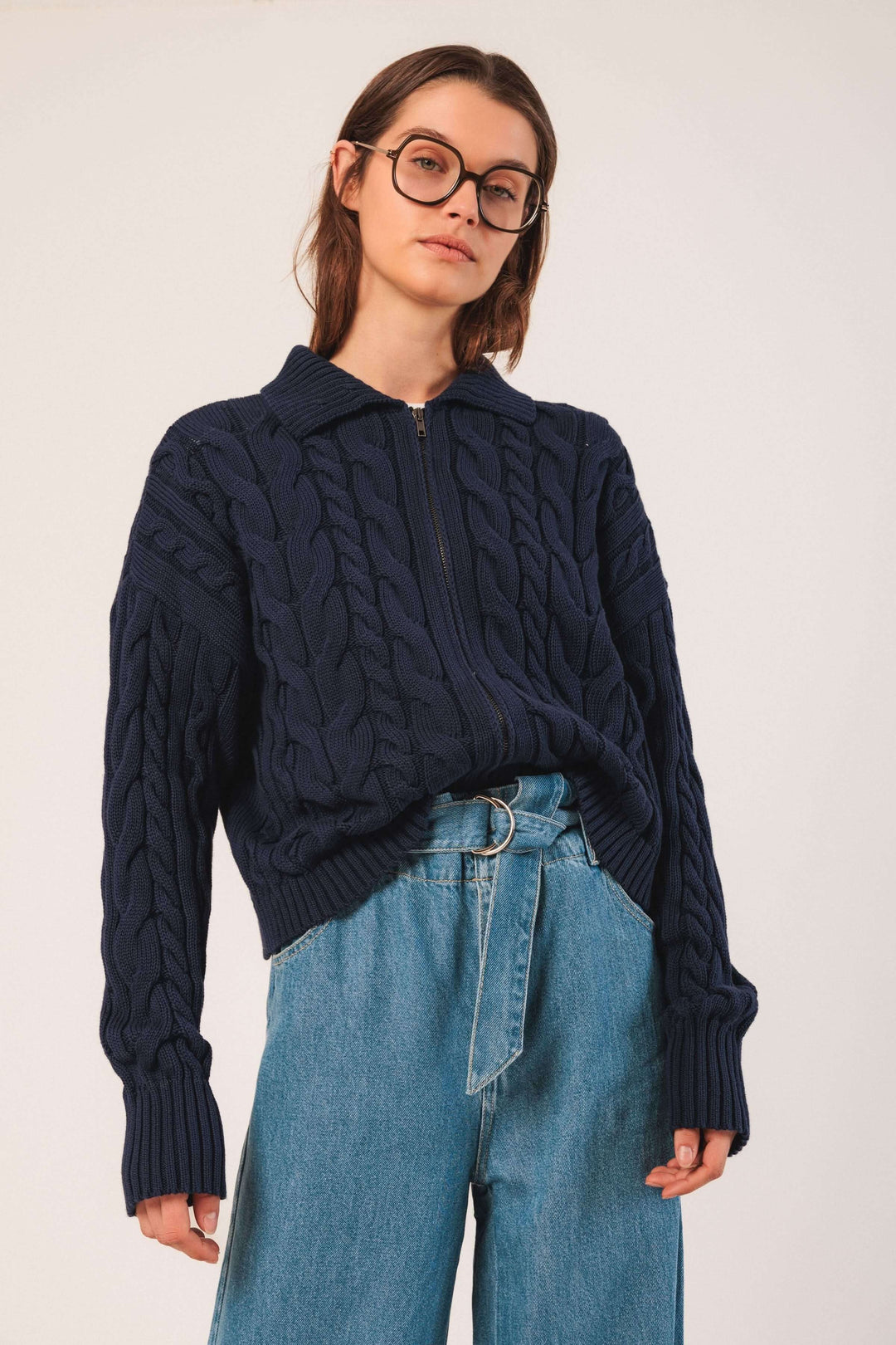 Cardigan à torsades en maille texturée avec col chemise et fermeture éclair, porté avec un jean taille haute.