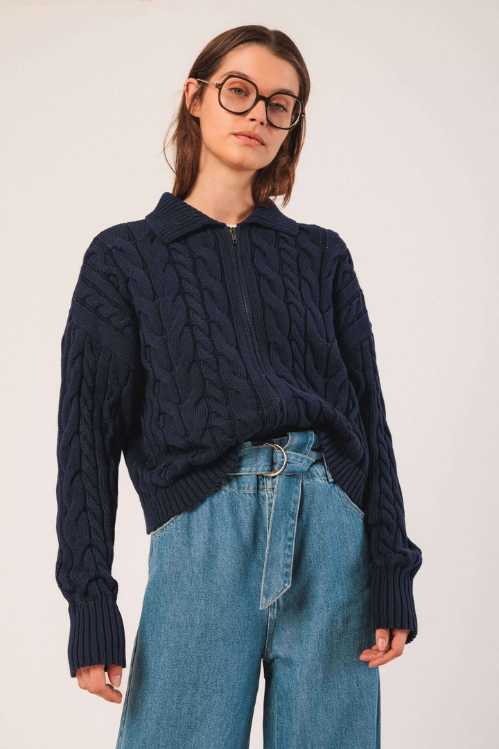 Cardigan à torsades en maille texturée avec col chemise et fermeture éclair, porté avec un jean taille haute.