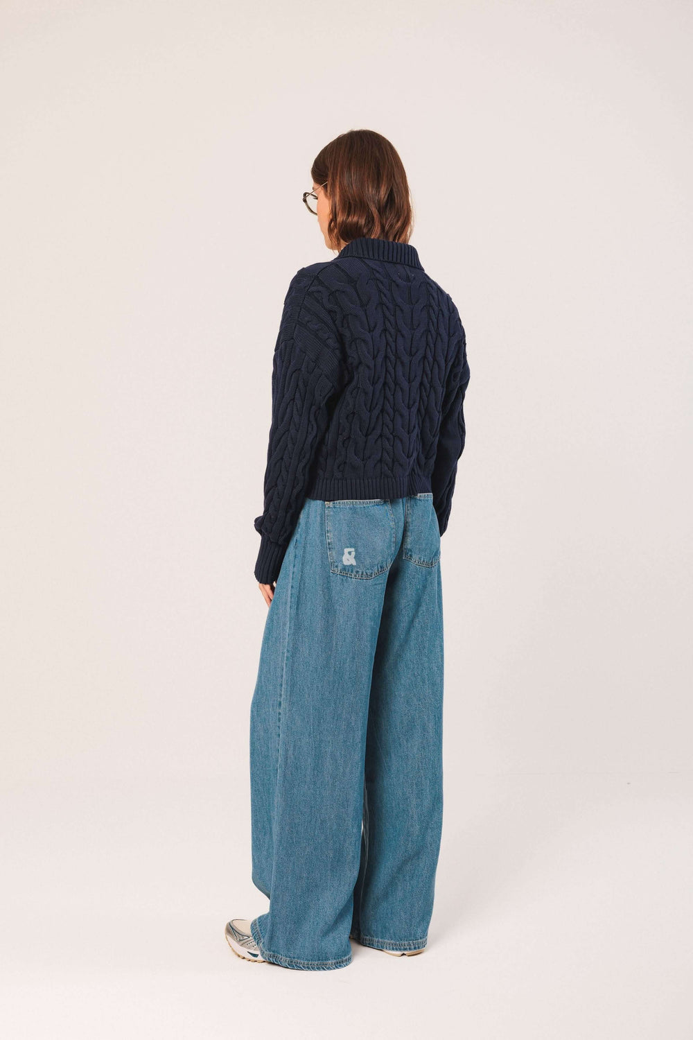 Femme de dos portant un cardigan à torsades bleu marine avec une coupe moderne, associé à un jean large.