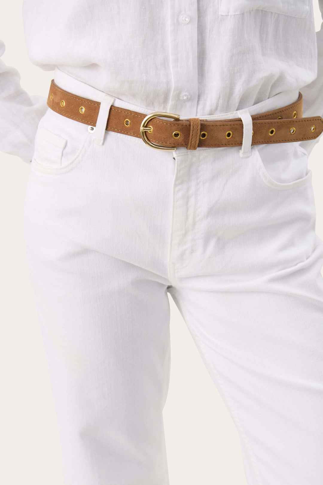 Ceinture Najad en suède avec œillets dorés, portée avec un jean blanc et chemise blanche.