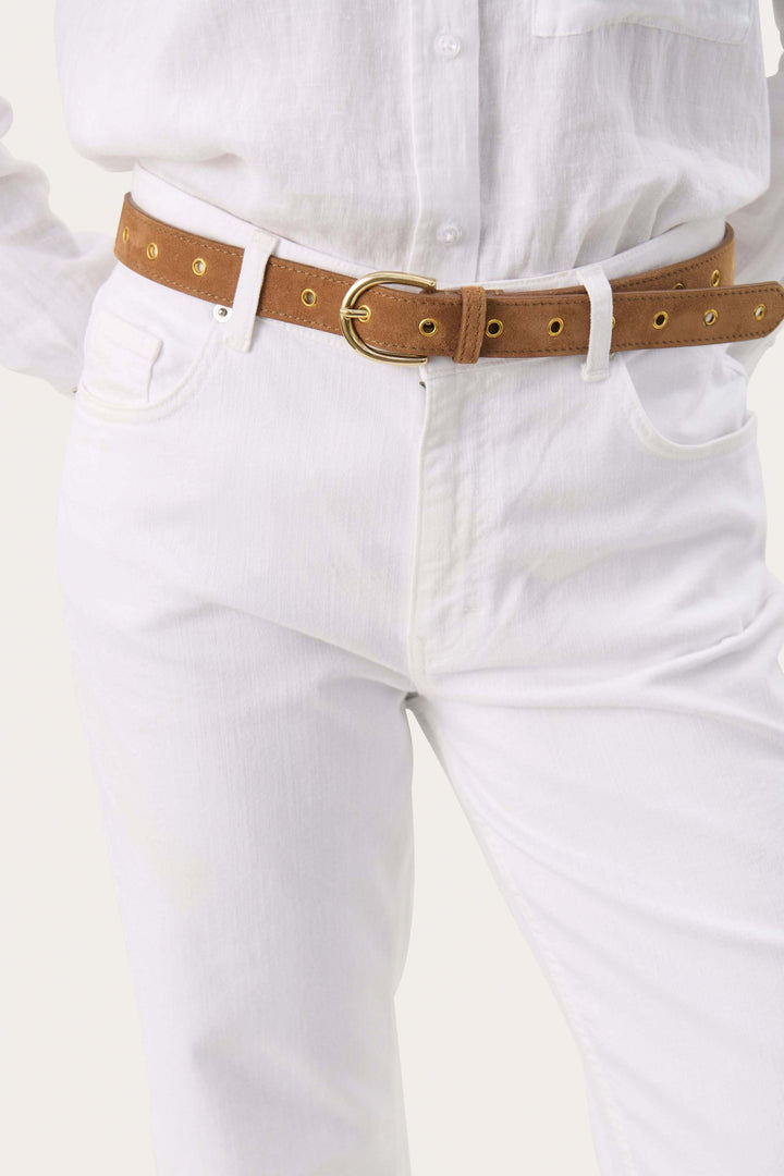 Ceinture Najad en suède avec œillets dorés, portée avec un jean blanc et chemise blanche.