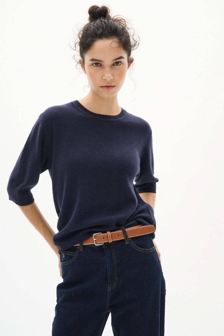 Femme portant un pull bleu marine et une ceinture en cuir lisse, ajoutant une touche classique à sa tenue.
