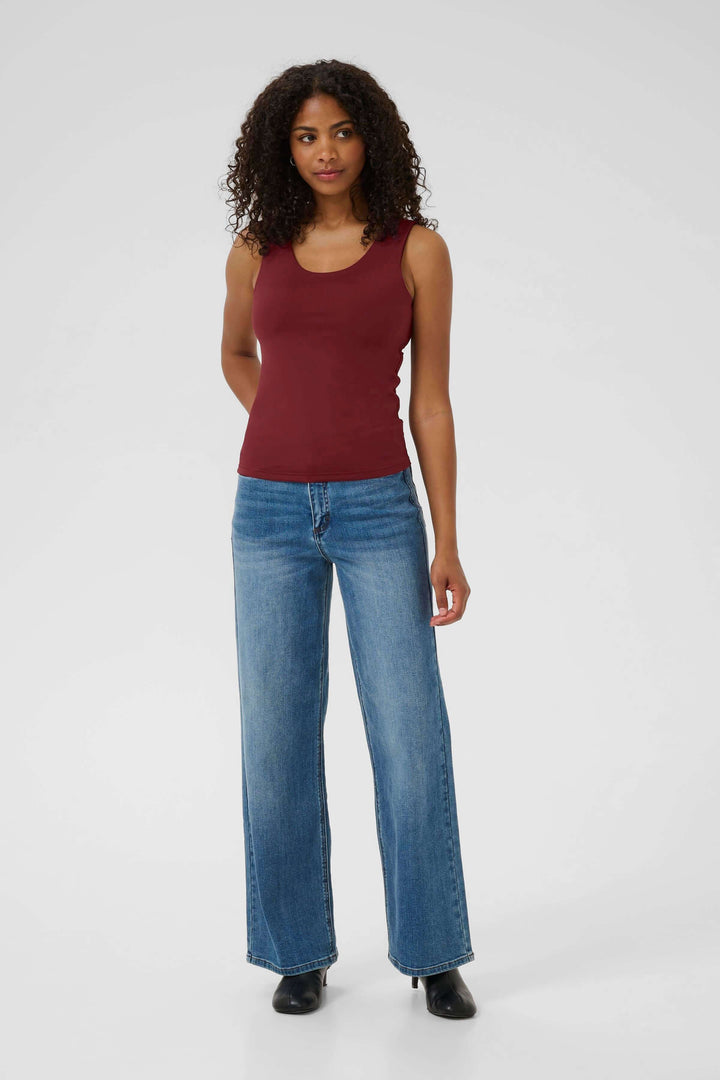 Femme portant un débardeur bordeaux avec un jean à jambes larges, posant debout, fond clair.