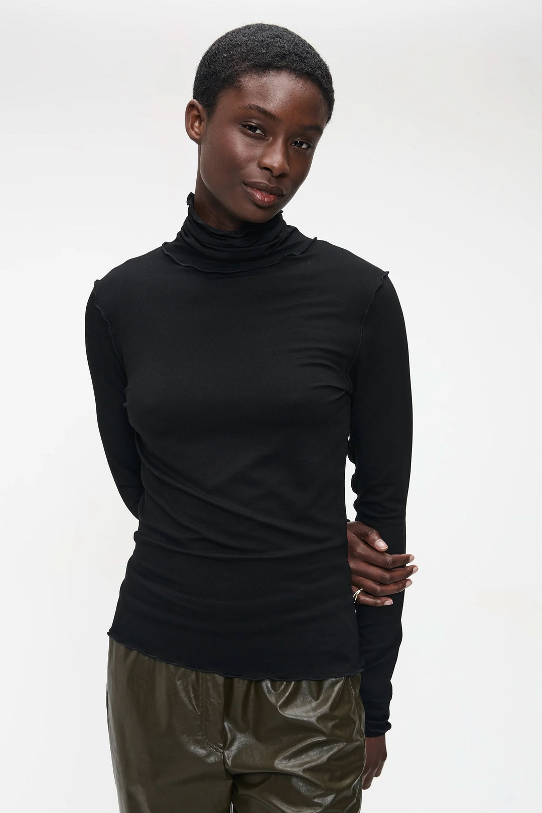 Chandail Janice noir à col roulé ajusté, style minimaliste, porté par un modèle avec pantalon vert.