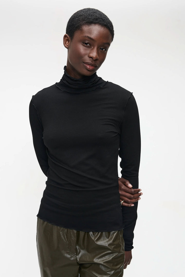 Chandail Janice noir à col roulé ajusté, style minimaliste, porté par un modèle avec pantalon vert.