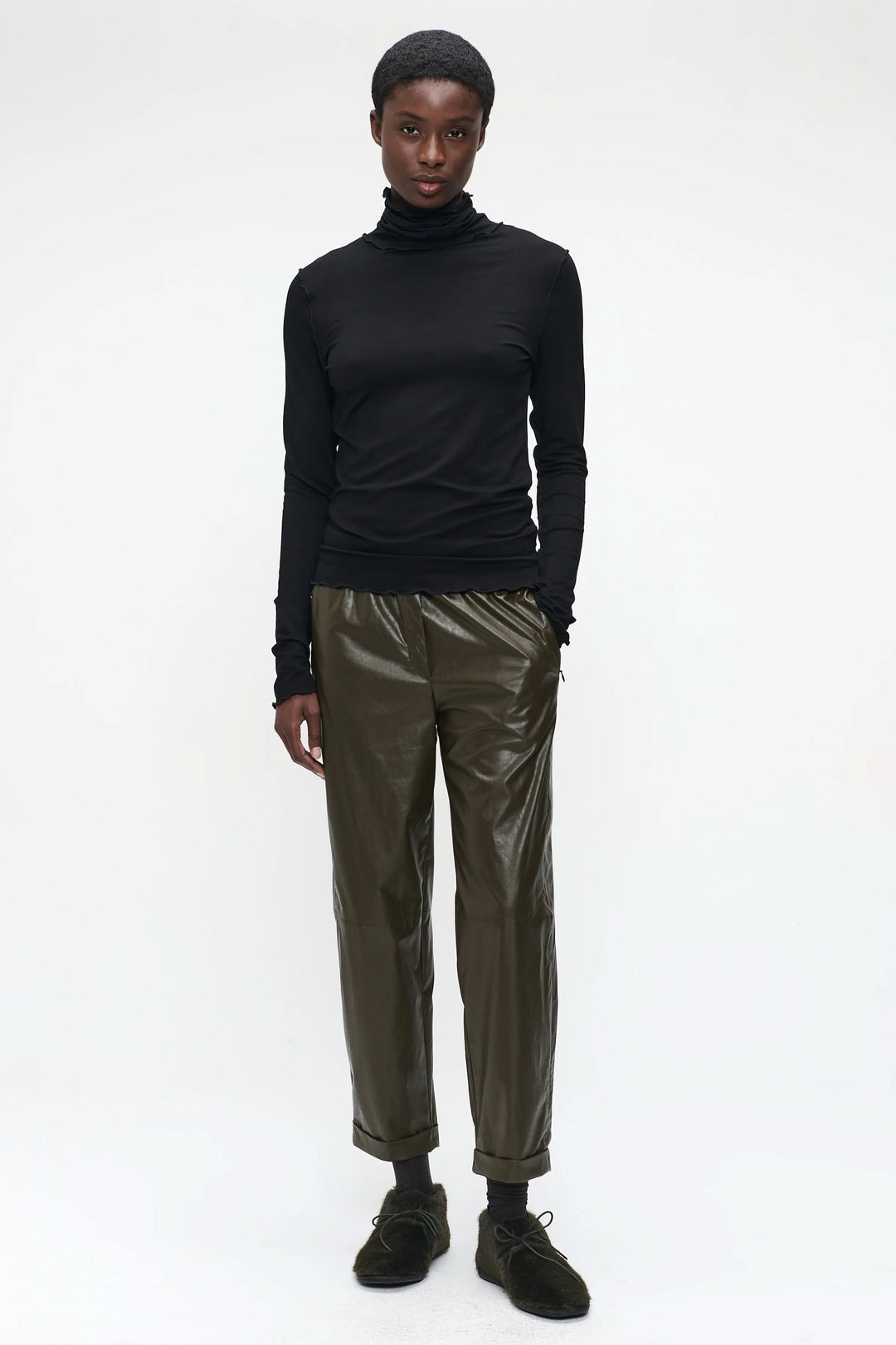 Chandail Janice noir ajusté avec col roulé, porté avec un pantalon vert olive pour un look minimaliste.