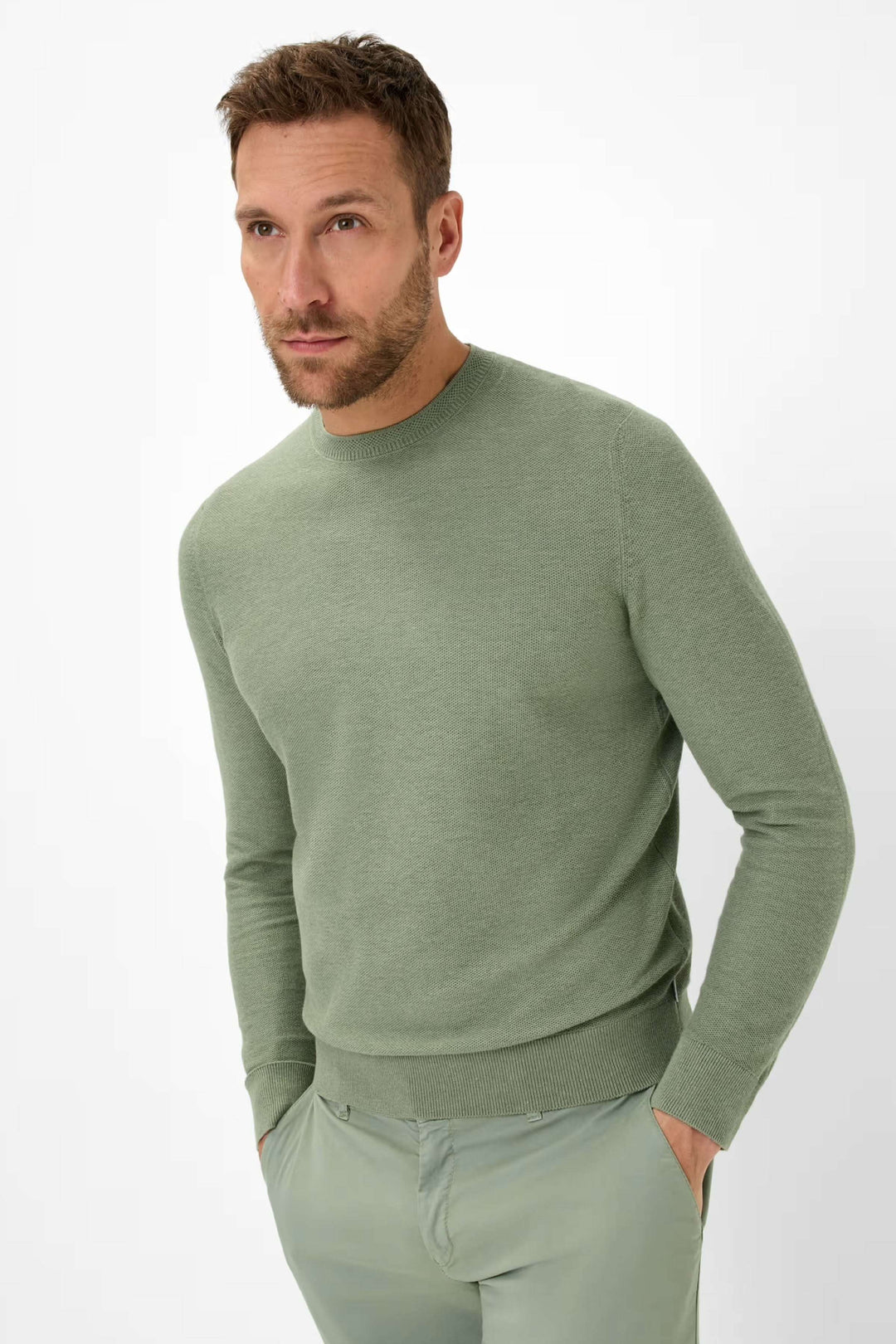 Homme portant un chandail à col rond en maille fine de couleur verte, associé à un pantalon clair.