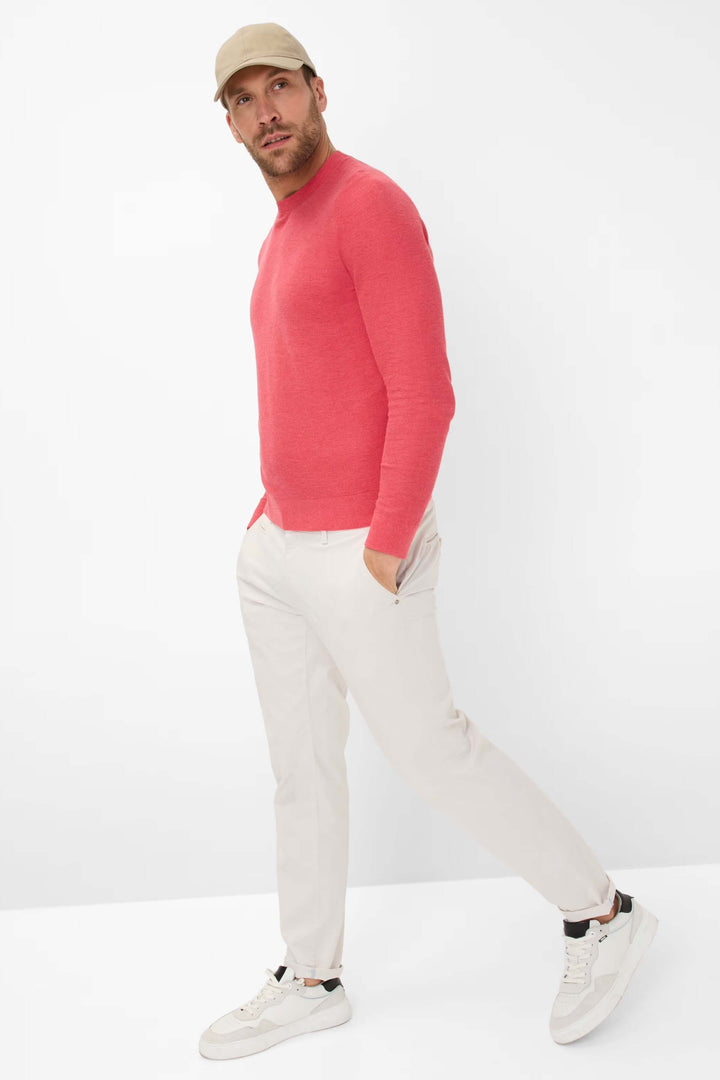 Homme portant un chandail à col rond rose avec un pantalon clair et des sneakers, style décontracté et élégant.