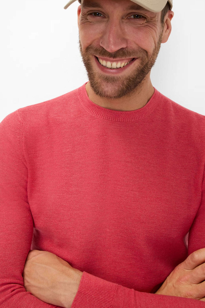 Homme souriant portant un chandail à col rond rose, parfait pour un style sobre et élégant.